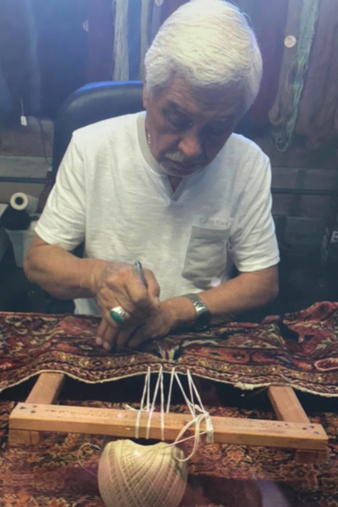 Mohammad Amin Rahmati, owner of Oriental Rug Care, started to learn from his father how to repair rugs at age 13 and almost 60 years later he continues the tradition in his Sequim shop. Here he intricately repairs a rug to make it appear as if no damage had been done. Photo courtesy of the Rahmati family