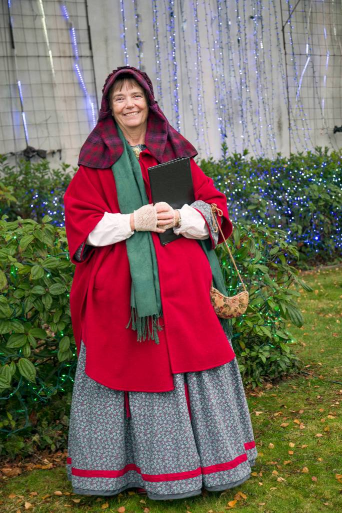 Karla Morgan, who says she loves historical re-enacting smiles in front of holiday lights in downtown Sequim during the Home Town Holidays event. She said the clothes resemble those worn by women in early to late Civil War times. No hoops, though, she said  too hard to drive in. Sequim Gazette photo by Emily Matthiessen