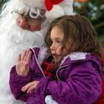 Noel Berra, age 4, waves from Sequim Santas lap at the Hometown Holidays, an usually annual event in Sequim. Although the day was gray and rainy, a spirit of good cheer was pervasive in the crowd who gathered at the Centennial Square on the corner of Washington Street and Sequim Avenue to listen to the Sequim City Orchestra play, buy hot drinks from the cub scouts and meet Santa and the Irrigation Festival Royalty. Peninsula Daily News photograph by Emily Matthiessen.