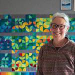 Fiber Artist Marla Varner stands in front of her temperature quilt. Each square is color coded to the high and low temperatures of each day of 2021 in her neighborhood in Sequim, with the smallest quarter circles signifying precipitation. Sequim Gazette photo by Emily Matthiessen