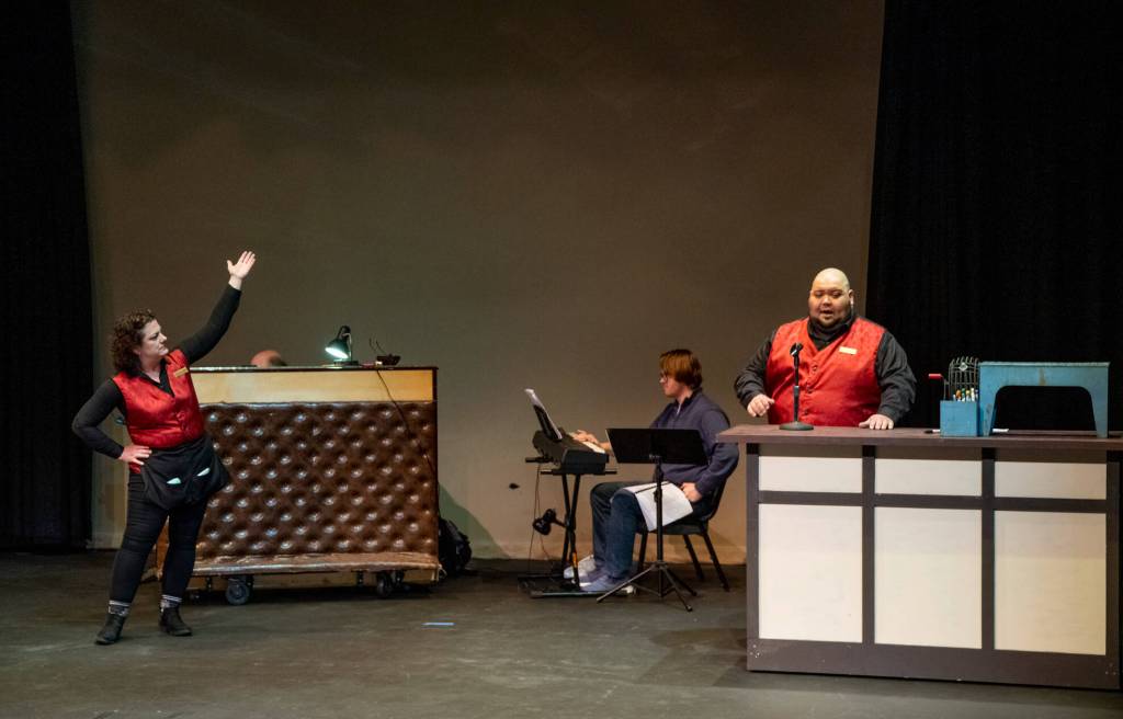 The brightness of the costumes of the bingo hall workers played by Jennifer Saul andMario Arruda contrasts with the drab colors of the bingo hall as they set the scene for an audience participation scene in Bingo A Winning Musical at Olympic Theatre Arts in Sequim. In the background, Port Angeles symphony violinist Morgan Bartholick plays the keyboard. Sequim Gazette photo by Emily Matthiessen