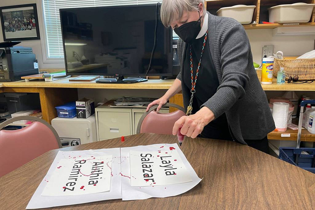 Sequim Gazette photo by Matthew Nash/ Rev. ClayOla Gitane, rector at St. Lukes Episcopal Church, spreads ink to symbolize the blood of two victims at the Uvalde, Texas school shooting. She displayed signs for the victims in front of the church.