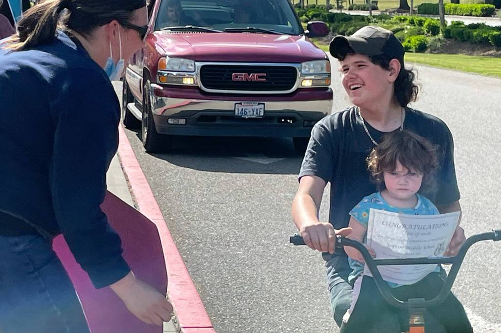 Sequim Gazette photo by Matthew Nash/ Teacher Shannon Paselk greets eighth grader William Young as he rides with his sister Zoie through Sequim Middle Schools drive-through event recognizing moving onto high school.