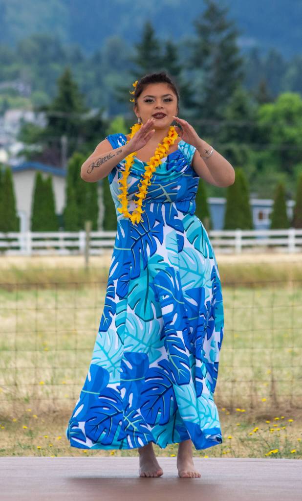 Sequim Gazette photo by Emily Matthiessen / Alakaʻi in training, Casara Desiree Hemakanamaikapu`uwai Caro leads members of a Sequim audience in a Hawaiian dance in the field behind the Sequim Library on July 16. Her mother, Candace Marie Kananiokamokihana Melendez of Hālau Hula Ka Lei Mokihana I Ka Ua Noe, plays the ukulele on the stage. North Olympic Library System hosted the dance, history and language workshop as part of their summer reading program.