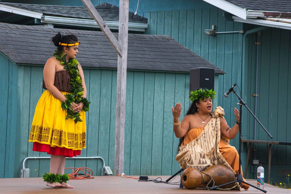 Sequim Gazette photo by Emily Matthiessen / Kumu Hula Mokihana Melendez of Hālau Hula Ka Lei Mokihana I Ka Ua Noe, shares wisdom, history and language with an audience behind the Sequim Library on July 16 as part of the North Olympic Librarys summer reading program. She began her formal training in hula at the age of five. Her daughter and featured dancer Alakai Makana Caro listens to her left.