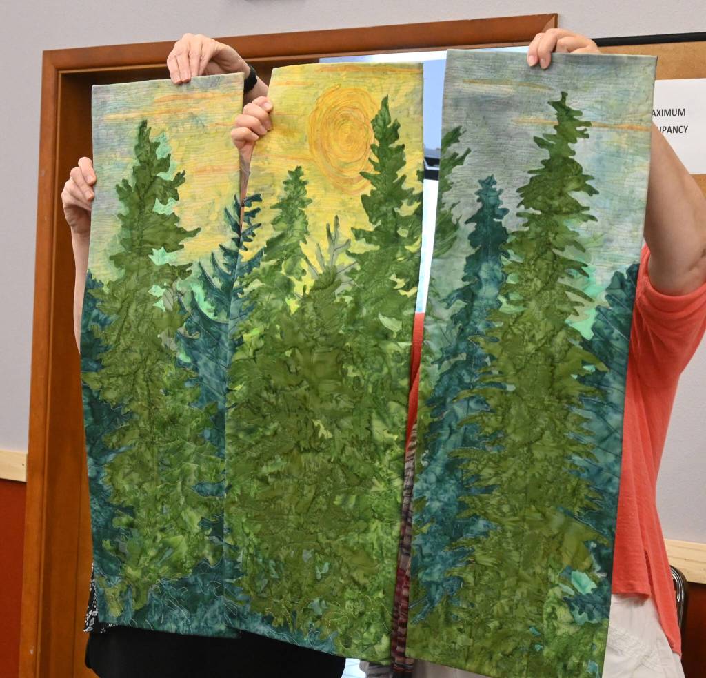 Sequim Gazette photo by Michael Dashiell / Sunbonnet Sue Quilt Club members hold up Anne Davies Summer Sunrise, which tied for first place in the clubs annual show for top art quilt (with Gladis Marrs Fiesta).