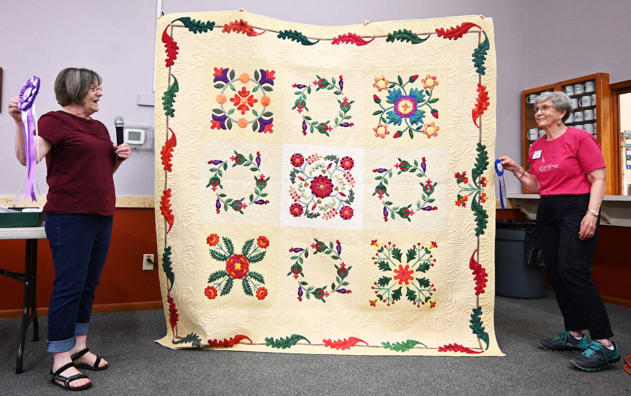 Sequim Gazette photo by Michael Dashiell / At left, Dawn Kerns  co-organizer of the Sunbonnet Sue Quilt Clubs annual show  presents Best in Show honors to Diane Davis for Emporia Rose Sampler on July 27 at the Sequim Masonic Temple. Davis also won the applique quilts division.