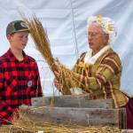 Sequim Gazette photo by Emily Matthiessen / Caleb Berneking assists Jane Ritchie, playing Martha Washington, as she demonstrates how flax was turned into linen in the 1700s to a crowd at the Northwest Colonial Festival last Friday.