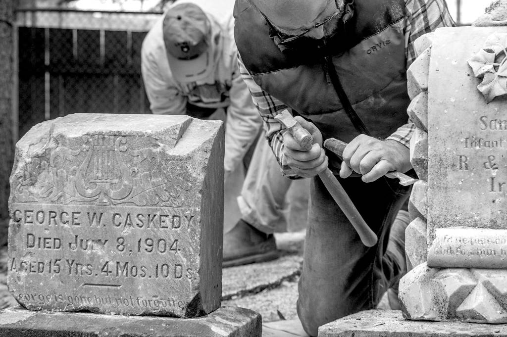 Sequim Gazette photo by Emily Matthiessen / Using a chisel and hammer, Chris Smith chips away white mortar from the headstone of the infant son of R. and Eleanor Irwin, in the corner of Pioneer Memorial Park. The photo, Gone by not forgotten, earned Emily Matthiessen a third place in the/W Feature, Portrait or Pictorial Photo division in the Washington Newspaper Publishers Associations 2022 Better Newspaper Contest.
