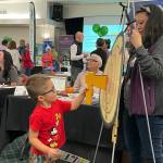 Sequim Gazette photo by Matthew Nash/ Noah Whitlock, 4, of Sequim tries his hand at the ax throw at Sound Publishings booth during the Business Showcase as Lara Stanton, multimedia advertising consultant, encourages him.
