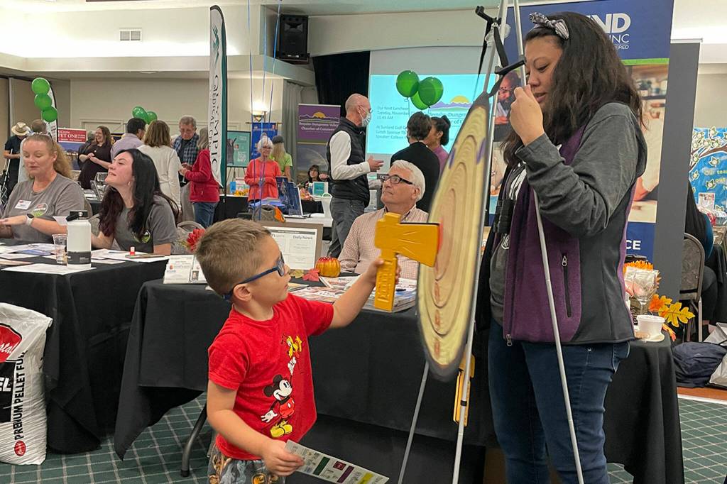 Sequim Gazette photo by Matthew Nash/ Noah Whitlock, 4, of Sequim tries his hand at the ax throw at Sound Publishings booth during the Business Showcase as Lara Stanton, multimedia advertising consultant, encourages him.