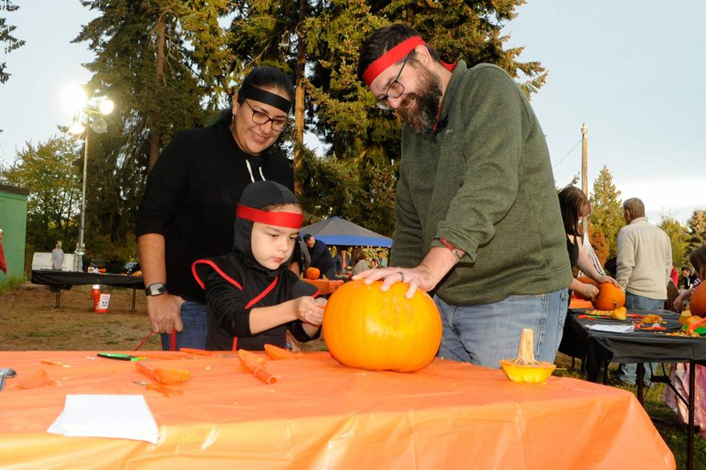 Sequim Gazette photo by Matthew Nash/ Six-year-old ninja Aiden Havel-Beristain carves a pumpkin with his ninja parents Gabriela Beristain-Havel and Tim Havel at the Sequim Prairie Granges Trunk-or-Treat on Oct. 29. For Halloween, Aiden said he loves Kit-Kats.