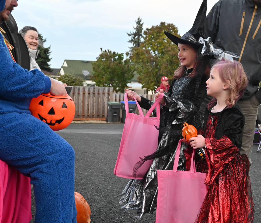 Sequim Gazette photo by Michael Dashiell / Ava, 7, and Ellie Schoessler, 4, talk with  and get some candy from  pastor Roger Stites at Faith Lutheran Churchs walk-through trunk-or-treat event on Oct. 31.
