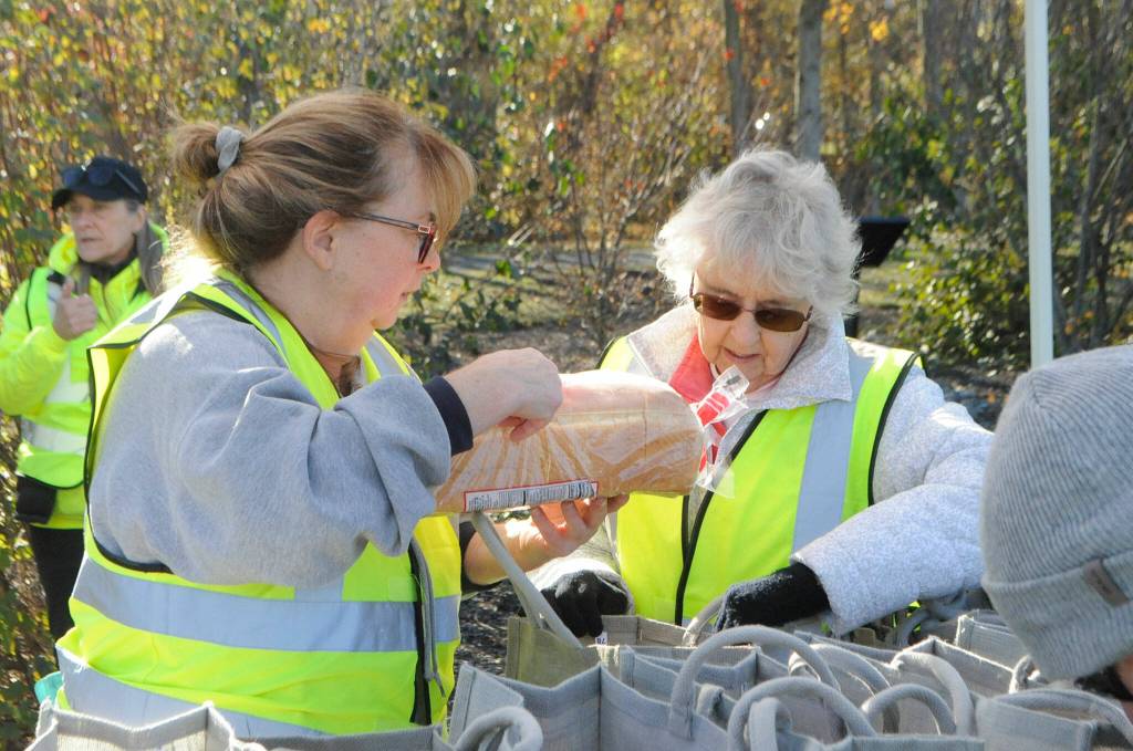 Sequim Gazette photo by Matthew Nash/ Karen Hill, left, with Dungeness Community Church, and Marge Swift help Sequim Sunrise Rotary members bag bread and other items for the Family Holiday Food Bag Distribution day.