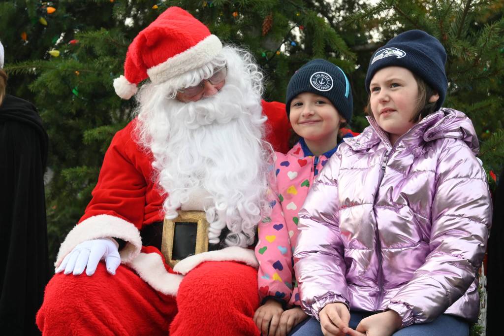 Sequim Gazette photo by Michael Dashiell / In middle, Liv Hanson, 8, and Zoey Hanson, 9, both of Sequim, talk with Santa Claus (Stephen Rosales) at the Hometown Holidays event Saturday afternoon in downtown Sequim.