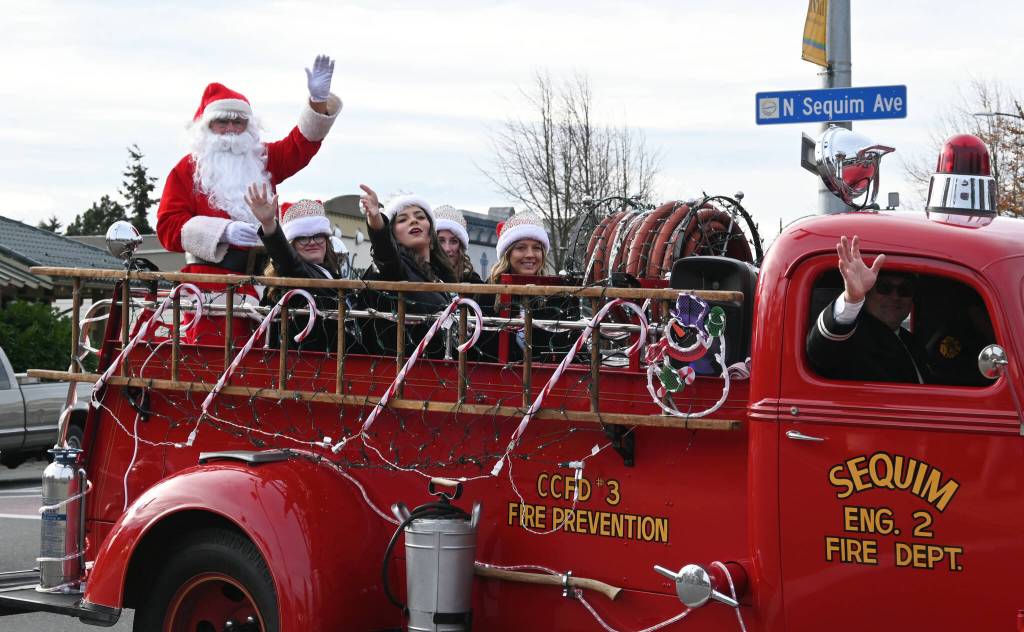 Sequim Gazette photo by Michael Dashiell / Santa Claus rides into downtown Sequim in a vintage fire engine as part of Saturdays Hometown Holidays event, accompanied by Sequim Irrigation Festival royalty: from left, princess Lauren Willis, queen Isabella Williams, and princesses Katherine Gould and Ellie Turner.