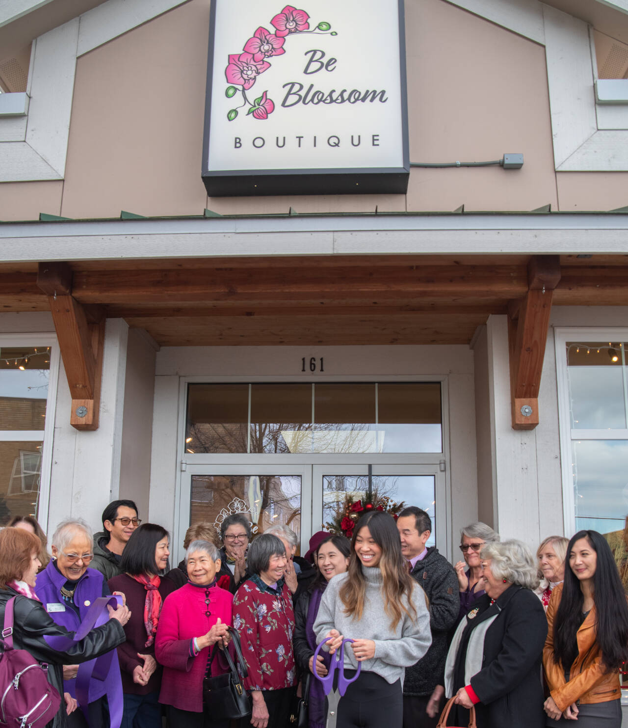 Sequim Gazette photo by Emily Matthiessen / Amanda He (holding scissors) beams in the midst of friends, family and Chamber of Commerce members at the grand opening of her womens and juniors clothing shop, Be Blossom Boutique, on Nov. 30.