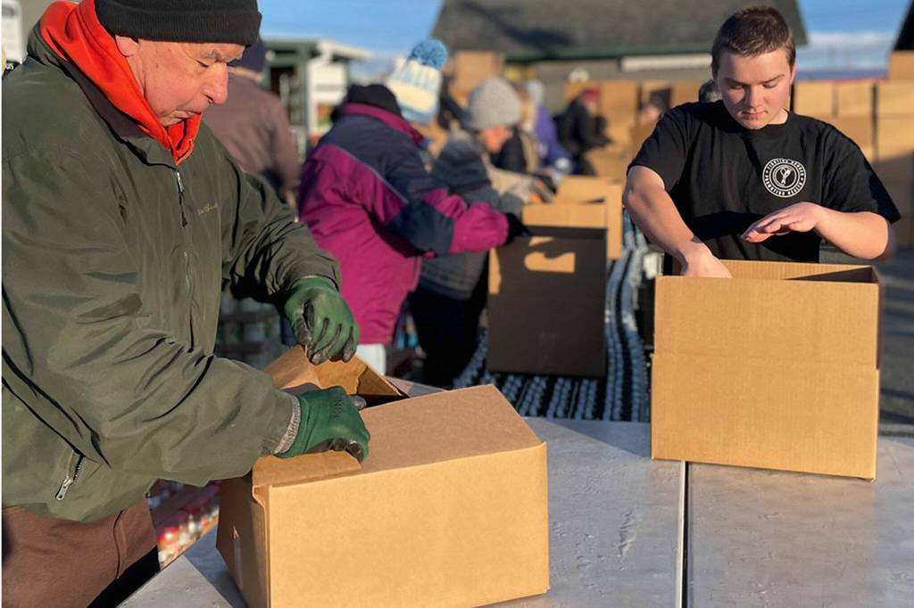 Sequim Gazette photo by Matthew Nash/ Bill Needham, a volunteer organizer for Sequim Seventh-day Adventist Church at Sequim Food Bank, and Chris Torell with Sequim Food Bank pack boxes on Dec. 15 for distribution in Carrie Blake Community Park for Christmas.