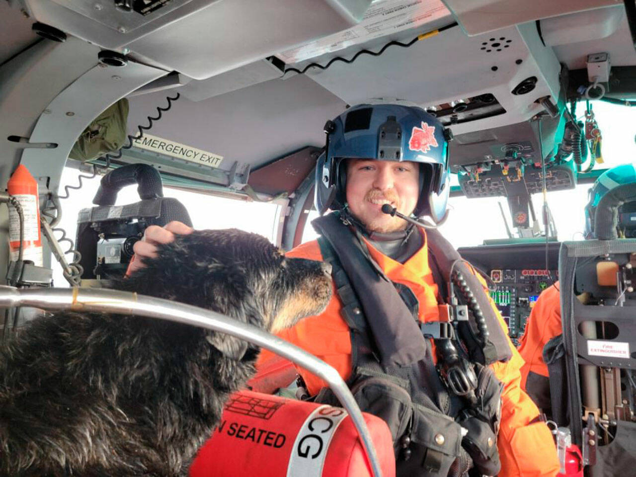 U.S. Coast Guard courtesy photo / Petty Officer 3rd Class Austen Marshall, an avionics electrical technician and a flight mechanic at Coast Guard Air Station Port Angeles, sits near a dog his aircrew rescued from a grounded sailing vessel near Vancouver Island, British Columbia. The aircrew rescued one person and two dogs from the vessel.