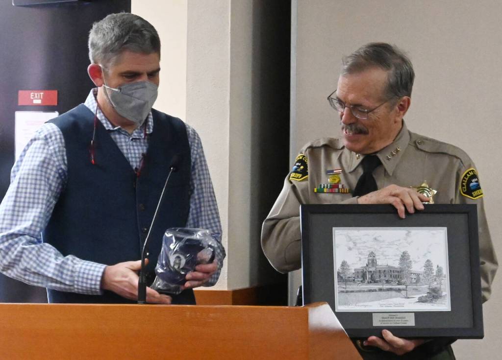 Outgoing Clallam County sheriff Bill Benedict, right, receives parting gifts from Clallam County Commissioner Mark Ozias at a special recognition presentation during a commissioners meeting in Port Angeles on Dec. 27.