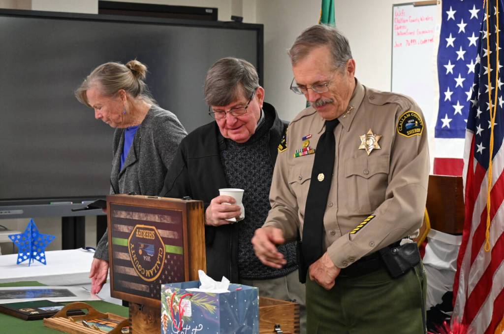 Sequim Gazette photos by Michael Dashiell 
Outgoing Clallam County sheriff Bill Benedict, right, looks at a variety of gifts and tributes at a retirement party on Dec. 27 in Port Angeles. Pictured with Benedict is wife Kathy and longtime friend Jack Flanagan.
