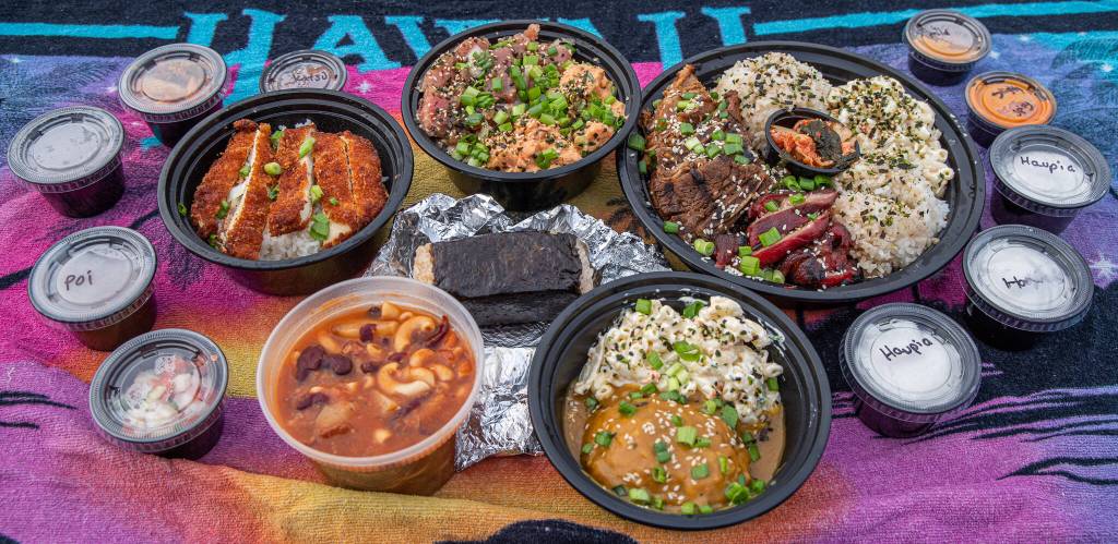 Sequim Gazette photo by Emily Matthiessen / Take out from Da Kindz Island Grill brings new flavors and smells to a chilly Pacific Northwest Day. The ring of big bowls, clockwise from top center: poke bowl with half spicy and half shoyu ahe and rice; barbacue mix plate with short ribs; chicken and char sui port; with rice and kim chee; vegetarian curry and rice with macaroni salad; Portuguese bean soup, and chicken katsu for keiki (children). In the middle is a portion of spam musubi, and surrounding the entrees are sides like haupia (coconut pudding), poi, kim chee and sauces.