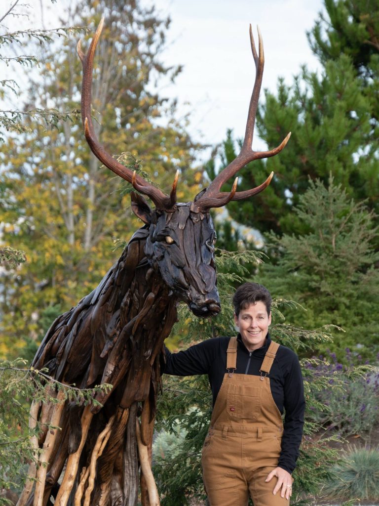 Photo courtesy of Molly Omann 
Olympic Peninsula artist Molly Omann stands near a 9-foot-tall elk she created from driftwood.