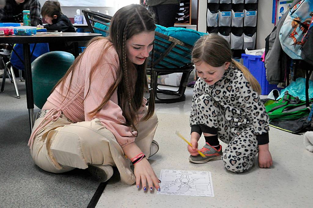 Sequim Gazette photo by Matthew Nash/ Eighth grader Ava Shinkle works with first grader Mavery Abken on a Dr. Seuss-inspired word work sheet on March 2 in Dawn Downs classroom at Greywolf Elementary. Sequim Middle School students traveled in the afternoon to read, draw and work with Greywolf students.