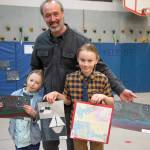 Sequim Gazette photo by Emily Matthiessen / Charlie Reno, kindergarten, left, and Stephen Jude Reno, 3rd grade, smile in the arms of their father, 5th grade math teacher Aaron Reno. The boys attended the after school art class Meet the Masters while Reno helped other children with math, with beautiful results. Its been pretty good, said Stephen. I like it - its been a lot of fun. Charlie agreed.