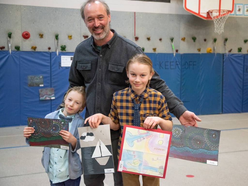 Sequim Gazette photo by Emily Matthiessen / Charlie Reno, kindergarten, left, and Stephen Jude Reno, 3rd grade, smile in the arms of their father, 5th grade math teacher Aaron Reno. The boys attended the after school art class Meet the Masters while Reno helped other children with math, with beautiful results. Its been pretty good, said Stephen. I like it - its been a lot of fun. Charlie agreed.