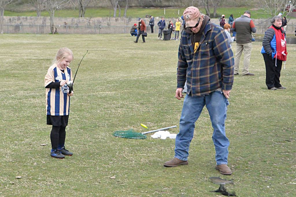 Sequim Gazette photo by Matthew Nash/ Zayleigh McCullem, 7, reels in a fish on April 22 with help from her dad Andy. She fished after a soccer game at the Albert Haller Playfields, and this was her second time fishing at Kids Fishing Day.
