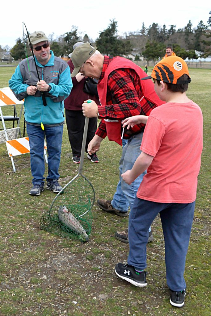 Sequim Gazette photo by Matthew Nash/ Dale Scheet and volunteer Robert Wilson help 11-year-old Paul Scheett take in a jumbo trout. This was Pauls fourth time fishing at Kids Fishing Day, he said.