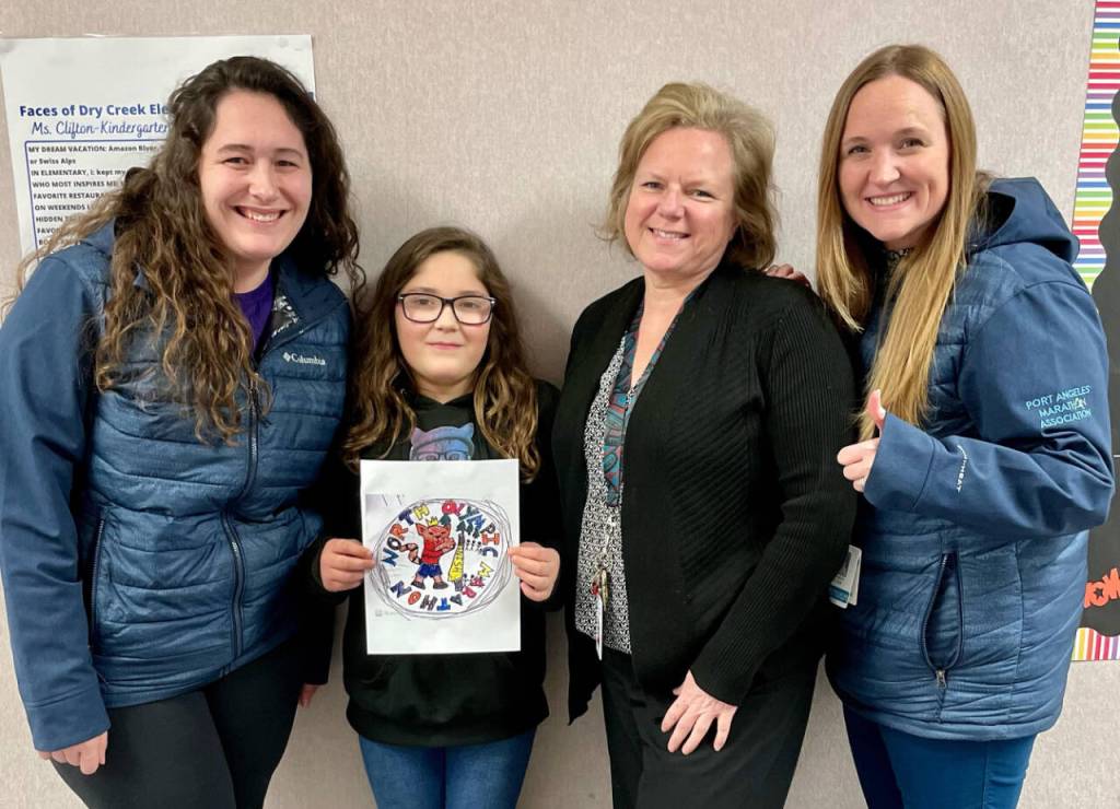 Photo courtesy of North Olympic Discovery Marathon / Dry Creek Elementary student Zoey Greene shows off her winning design in the 2023 North Olympic Discovery Marathon (NODM) Kids Medal Design Contest. Pictured with Greene are, from left, NODM board member Kaitlin Buckmaster, Dry Creek principal Julie Bryant and NODM board member Carmen Geyer.