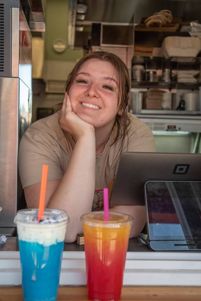 Sequim Gazette photo by Emily Matthiessen 
Grace Titterness smiles at the walk-up window of Country Coffee and Grub with her drink creations: Sunrise, pineberry and white peach with mango nectar, and The Thunderstorm, blue raspberry and blue caracao with coconut cold foam, topped with blue spirulina powder and a pea flower.