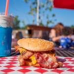 In the background a local family enjoys their first lunch at Country Coffee and Grub while in the foreground a Western Bacon Cheeseburger and The Thunderstorm (blue raspberry and blue caracao and coconut cold cream with blue spirulina powder and a pea flower), wait to be consumed.