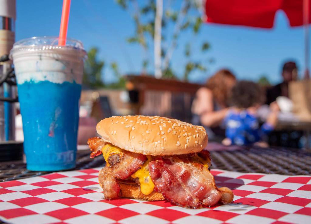 In the background a local family enjoys their first lunch at Country Coffee and Grub while in the foreground a Western Bacon Cheeseburger and The Thunderstorm (blue raspberry and blue caracao and coconut cold cream with blue spirulina powder and a pea flower), wait to be consumed.