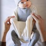 The CozeeCoo holds a babys arms in a loop so that they cant reach above their chest but can still move their arms, elbows, hips and legs.