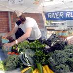 Keith Thorpe/Peninsula Daily News Ben Rutherford, an employee of River Run Farms near Sequim, arranges locally-grown produce at the Port Angeles Farmers Market on Saturday.