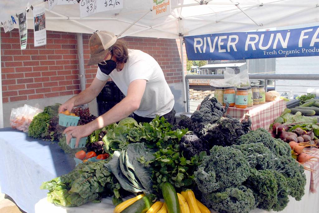 Keith Thorpe/Peninsula Daily News Ben Rutherford, an employee of River Run Farms near Sequim, arranges locally-grown produce at the Port Angeles Farmers Market on Saturday.