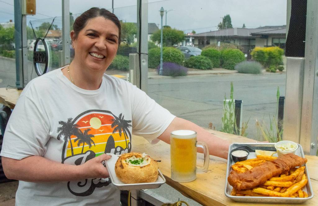 Sequim Gazette photo by Emily Matthiessen / Long-term employee Maria Flores-Lewis serves a helping of clam chowder in a bread bowl and fish and chips with coleslaw and tartar sauce in the outside seating area of FnChips. Maria is amphibious, say Salty Girls owners Tracie Millet and Lavon Gomes, she helps wherever she is needed. The owners say that employees high morale is the force behind Salty Girls success.