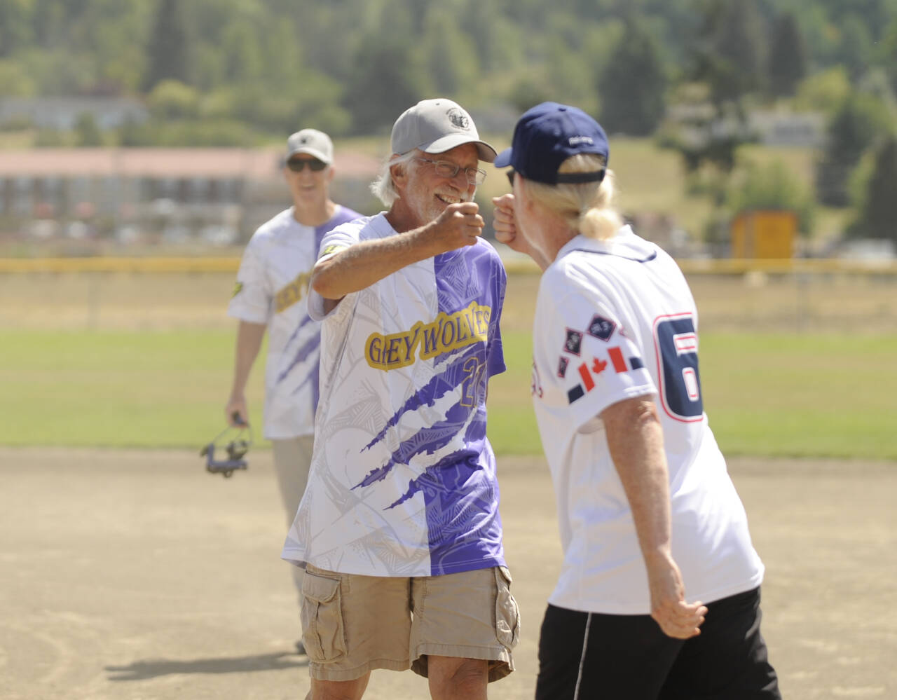 Sequim Greywolves Joel Hecht, center, bumps fists with a Victoria Raiders player after their clubs first friendly softball match-up on July 8 at Carrie Blake Community Park. Behind Hecht is teammate David Pugsley.