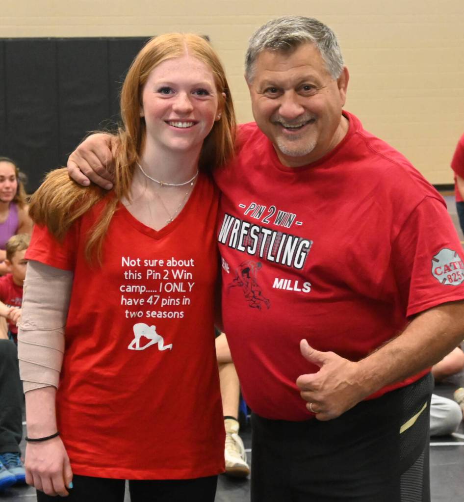Mya Herrera, a standout wrestler at Cascade High School (Leavenworth), shares a moment with former NCAA champ Gene Mills ant a wrestling camp in Sequim last week. Herrera, donning a shirt she made for the camp (as she did at the 2022 camp), suffered hyperextended arm on the camps first day but expects to be ready to go in the late fall for her season. She placed third in the 205 weight class (girls 1B/2B/1A/2A) division at MatClassic as a junior in 2022-23.