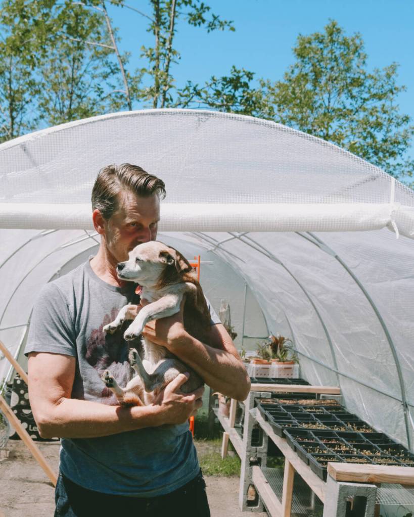 Photo courtesy of Sequim Farmers & Artisans Market (SFAM) / David Wilson and his dog outside of the greenhouse where Wilson finishes off his microgreens.