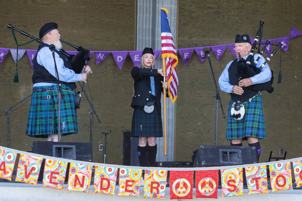 Sequim Gazette photo by Emily Matthiessen / Erick Evans, left, and Dr. Mack (Tom McCurdy), right, with their apprentice Heidi Slack holding the flag, play the bagpipes for the street festival crowd on opening day at Carrie Blake Park.