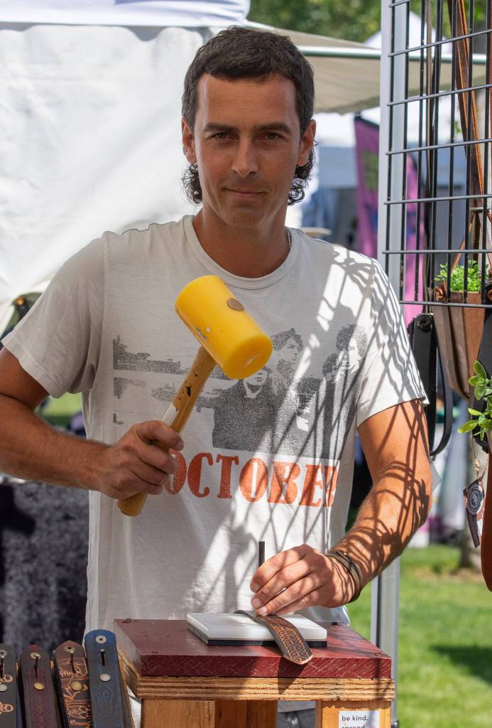 Sequim Gazette photo by Emily Matthiessen / Hunter Patterson of Marakesh Leather makes holes in a custom belt at the Lavender Street Festival in Carrie Blake. Pattersons family has sold leather belts and other items at the Pike Street Market since 1971.