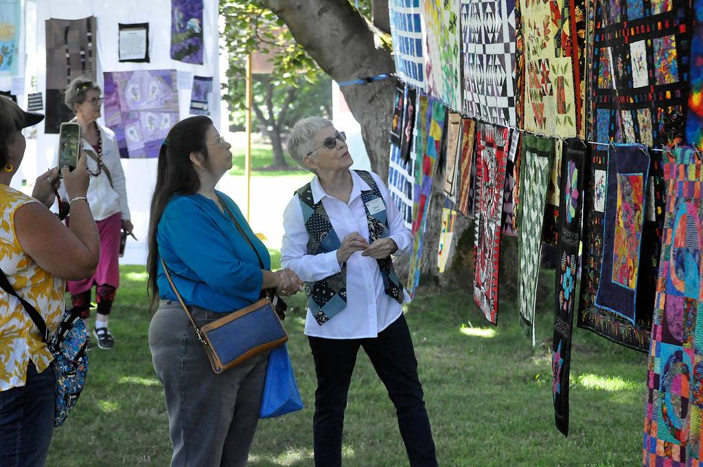 Sequim Gazette photo by Matthew Nash/ Janet Lenfant, this years featured quilter on right, speaks with Bertha Beattie of Port Angeles as her sister-in-law Susi Beattie of Sequim snaps a photo. Lenfant had 25-plus quilts and various bags shes made on display at the Sunbonnet Sue Quilt Clubs annual show on July 22.
