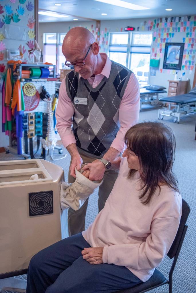 Photo by Emily Matthiessen / Aaron Staeben takes Sandy Pufky-Neguss arm out of a Fluidotherapy dry whirlpool heat treatment during an occupational therapy appointment at Sequims Peak Performance Therapy Center.