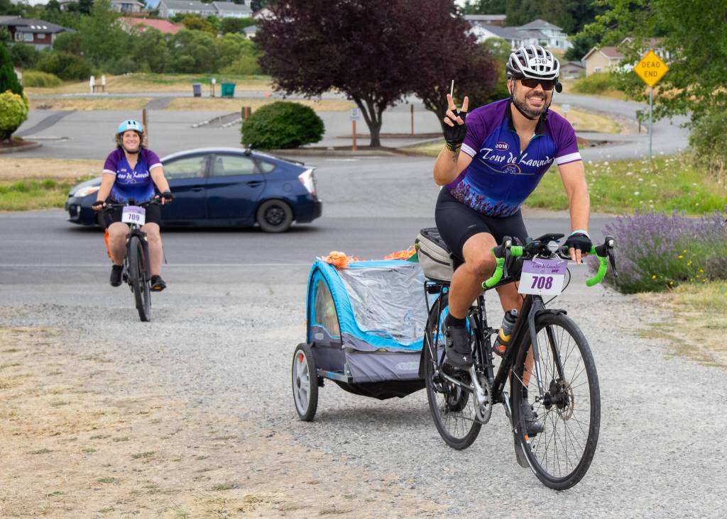Sequim Gazette Photo by Emily Matthiessen / Stephen Fisher, from the Kenmore area, towing two-year-old Juniper and the pugs Jackie and JoJo, with wife Catherine Creason following, participated in the couples sixth Tour de Lavender this weekend. Creason said that they were married during the event 5 years ago.