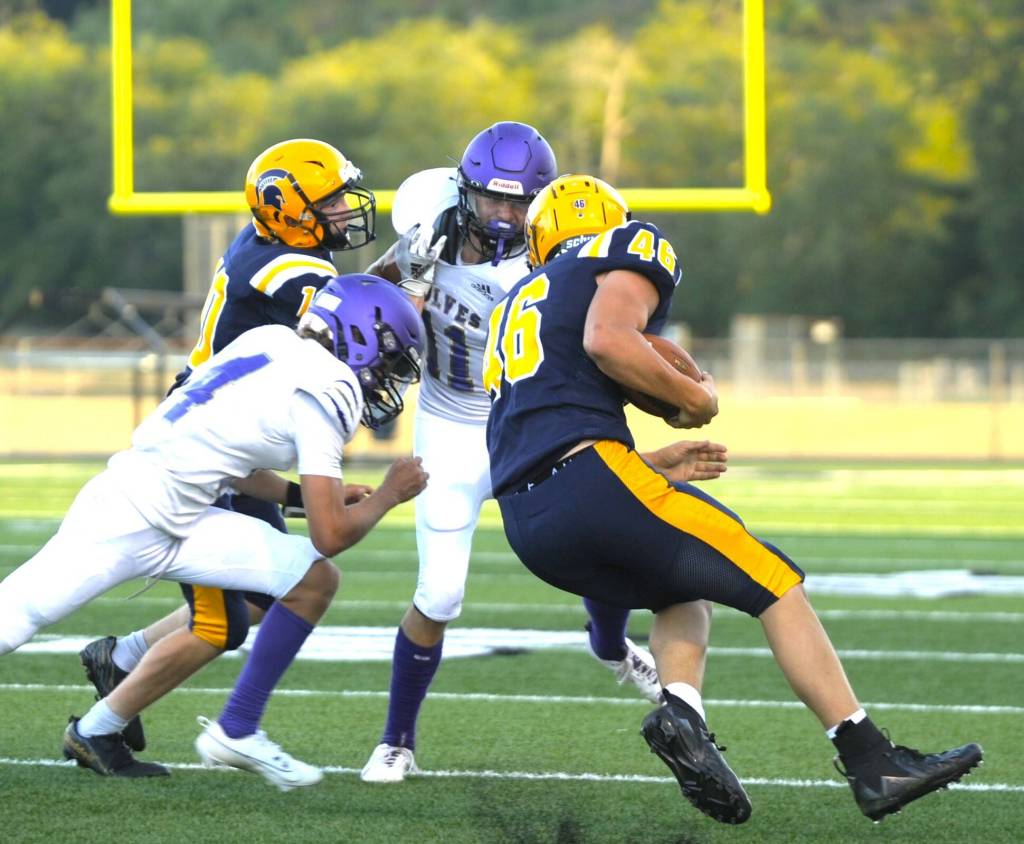 Sequim Gazette photo by Michael Dashiell / Sequim's Charlie Grider (11) and James Mason look to take down Forks running back Brody Lausche in the first half of the Wolves' season-opener at Forks on Sept. 1.