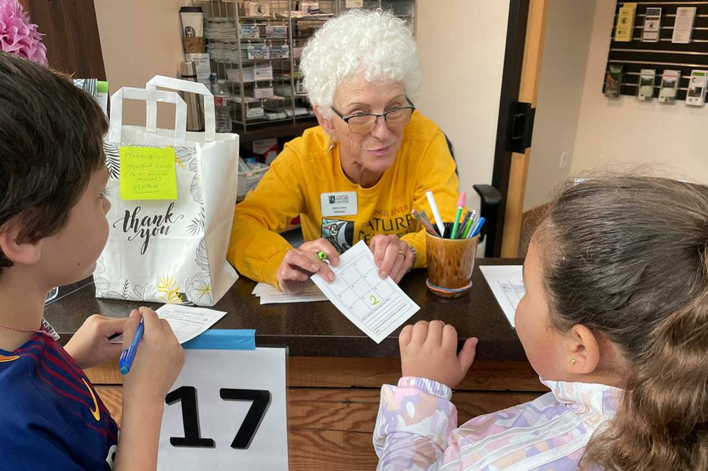 Sequim Gazette photo by Matthew Nash/ Gretha Davis greets third graders Andre Turner and Leilanie Arellano Gallengos at the information Booth inside the Dungeness River Nature Center on Sept. 22. Students could get passports during the festival to visit different booths to receive stamps and a chance to win a prize. Davis asked students how many times theyve visited the center.